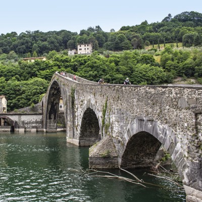 Fietsers op een historische stenen boogbrug over een rivier in Toscane, Italië.