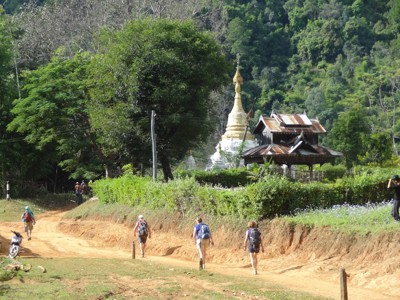 Wandelaars op een zandpad langs een pagode in het groene heuvellandschap van Myanmar.