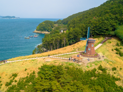 Windmolen op een heuvel aan de kust van Zuid-Korea, met uitzicht op zee en bosrijke kliffen.