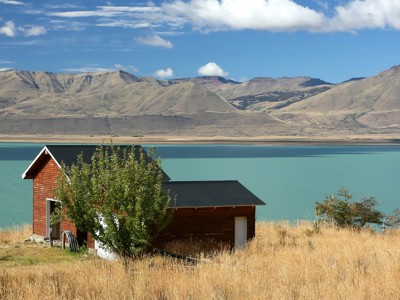 Houten huisje aan een turkoois meer met berglandschap op de achtergrond in Patagonië, Argentinië.
