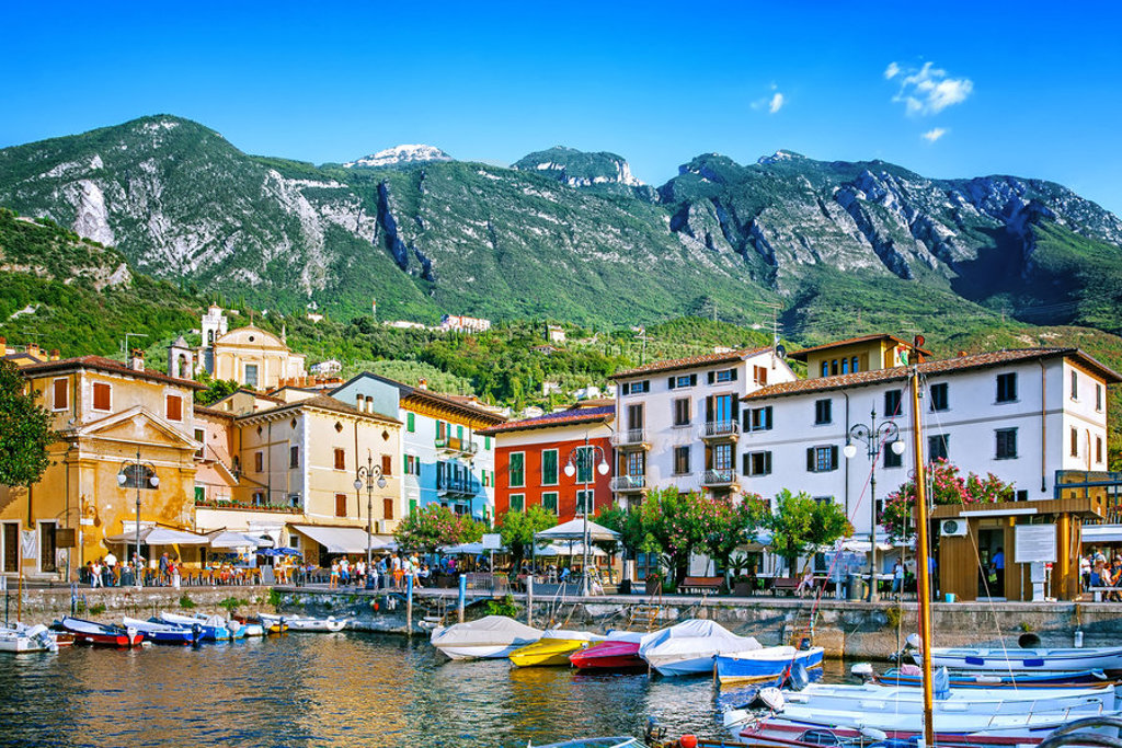 Haven met kleurrijke huizen en bootjes aan het Gardameer in Italië, met bergen op de achtergrond.
