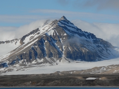 Berglandschap op Spitsbergen met besneeuwde bergtop en gletsjer onder een blauwe lucht.