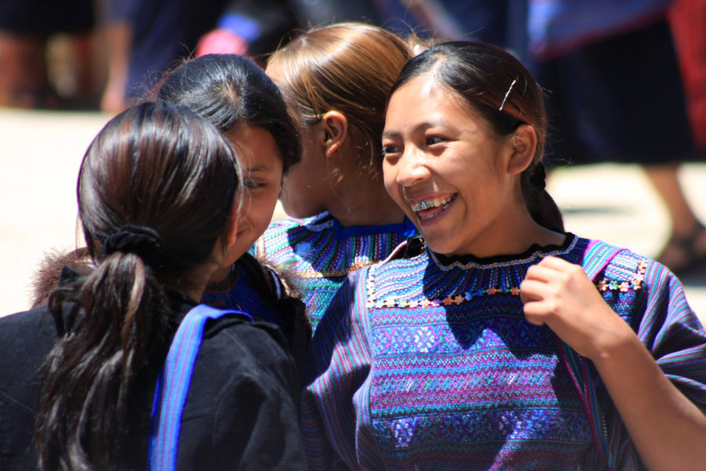 Jonge vrouwen in kleurrijke traditionele kleding praten en lachen tijdens een marktbezoek in Guatemala.