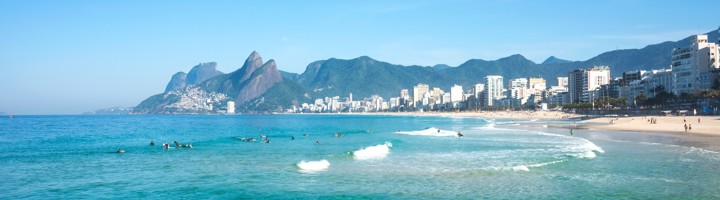 Panorama van Ipanema Beach in Rio de Janeiro met golven, strand, skyline en bergen op de achtergrond.
