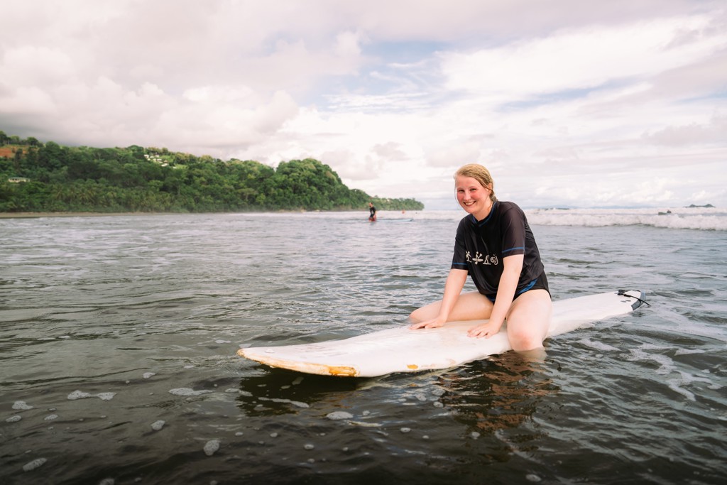 Jonge reiziger op surfplank in de zee bij Costa Rica tijdens een 22-35ers groepsreis.