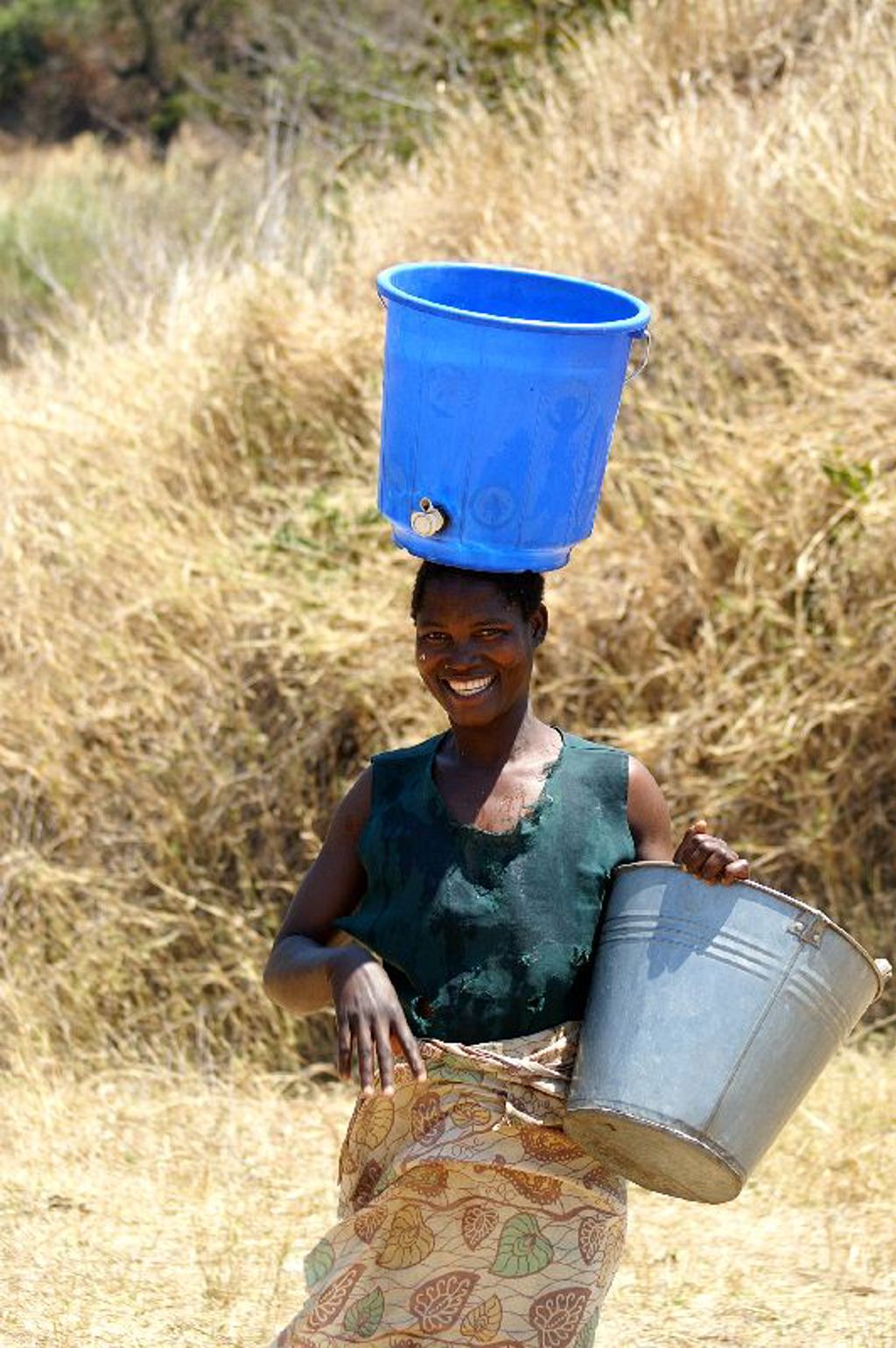 Vrouw in Malawi met emmer en blauwe waterton op haar hoofd, tijdens groepsrondreis Zambia, Malawi en Tanzania.