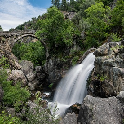Stenen boogbrug bij waterval in Peneda-Gerês National Park tijdens wandeling.