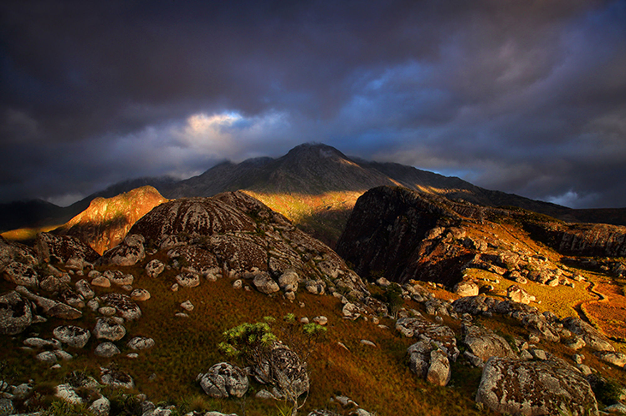 Berglandschap met rotsen en zonlicht onder donkere wolken.