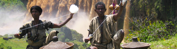 Ethiopische muzikanten spelen traditionele snaarinstrumenten bij een waterval.