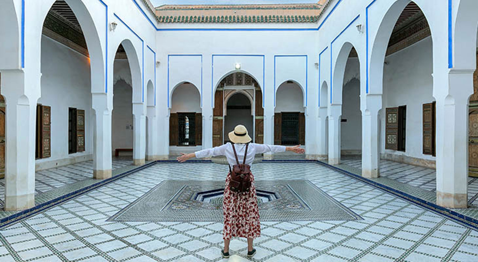 Bahia paleis Toerist in Marokkaanse riad binnenplaats met mozaïektegels, bogen en fontein.