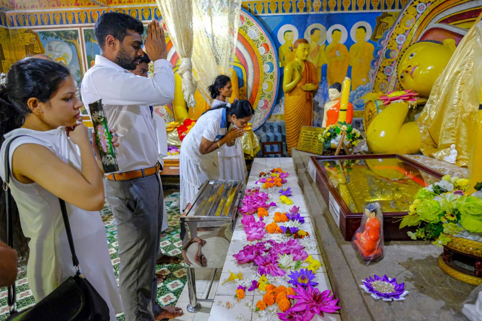 Bezoekers bidden bij een liggende Boeddha in een kleurrijke tempel in Sri Lanka.