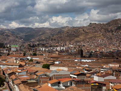 Uitzicht over Cusco met roodbruine daken en berghellingen onder dreigende wolkenlucht.