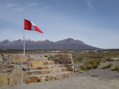 Peruaanse vlag bij een stenen uitkijkpunt met Andesgebergte op de achtergrond.