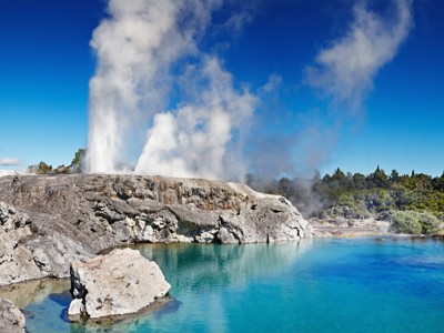 Stoompluimen bij een geiser en helderblauw thermaal meer in Rotorua, Nieuw-Zeeland.