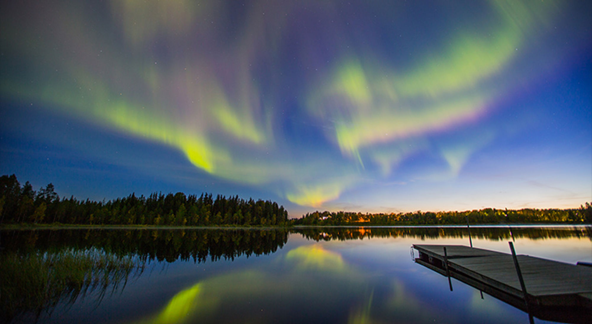 Noorderlicht in Kiruna, Zweden Noorderlicht boven een rustig meer met steiger, weerspiegeld in het water.