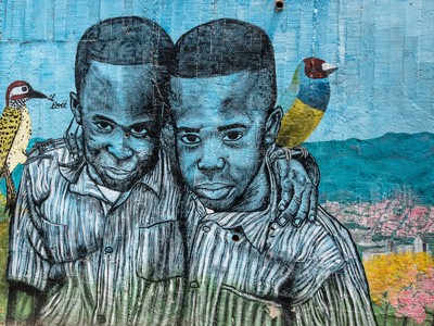 Muurschildering van twee jongens met vogels op een blauwe muur in Colombia, Route Colombia.