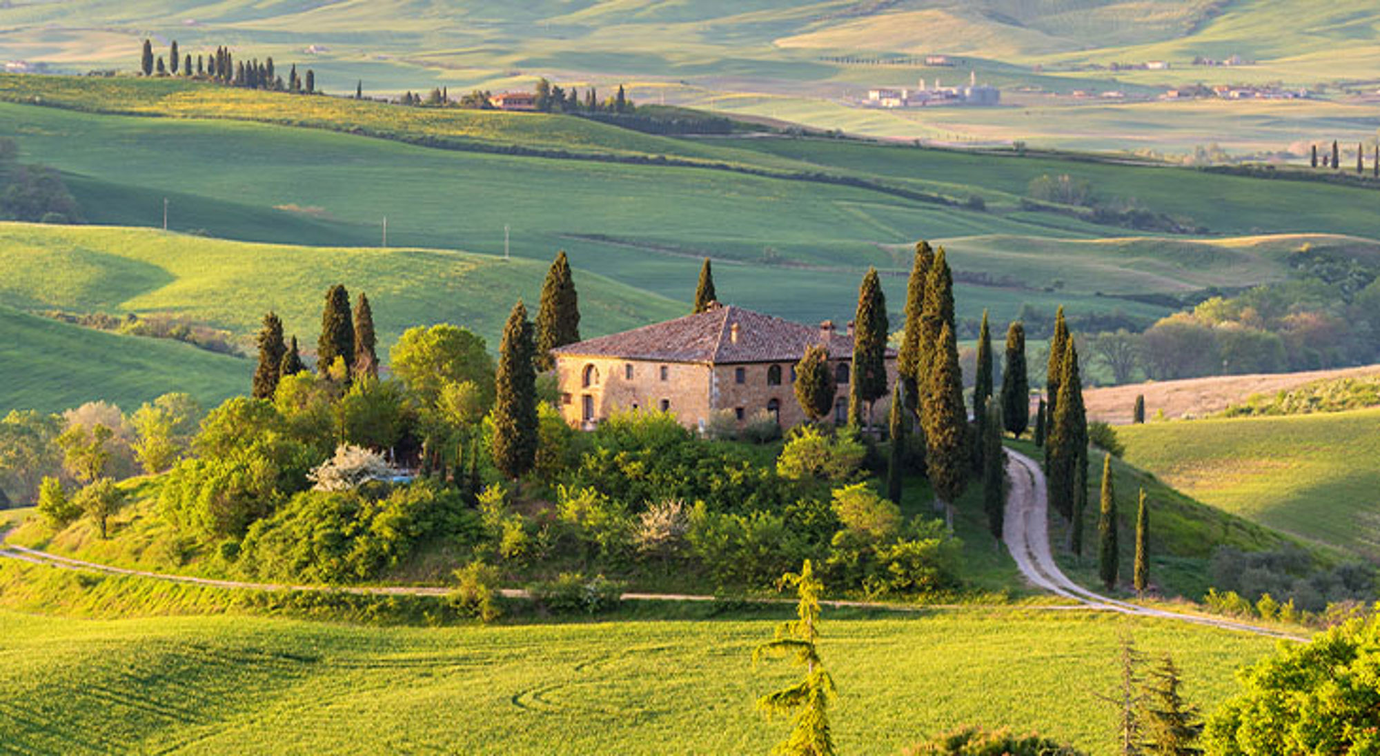 Toscane Landhuis tussen glooiende heuvels met cipressen en kronkelweg, ideaal decor voor fietsvakanties met Sawadee.
