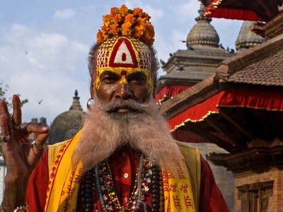 Sadhu met beschilderd gezicht en bloemenkrans bij een tempelcomplex in Nepal tijdens de route India en Nepal.