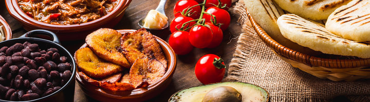 Zuid-Amerikaanse gerechten met zwarte bonen, gebakken bakbanaan, avocado, tomaten en arepas op tafel.