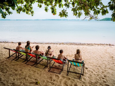 Kinderen relaxen op strandstoelen onder bomen aan zee in Thailand tijdens de Route Thailand 15 dagen.
