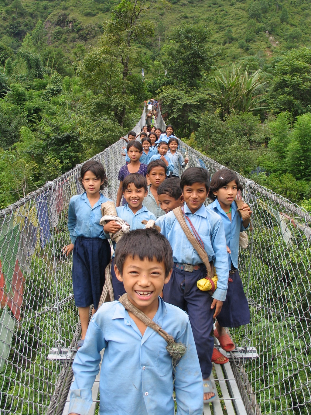 Nepalese schoolkinderen steken een hangbrug over in een groene vallei tijdens een familiereis door Nepal.