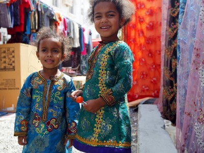 Twee lachende kinderen in kleurrijke kleding op een markt in Oman, tijdens een groepsrondreis Oman en Dubai.