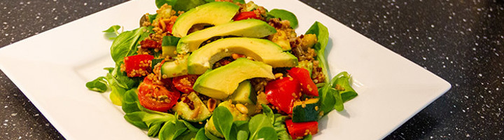 Quinoasalade met avocado, tomaat, komkommer en veldsla op een wit bord.
