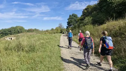 Groepsreis in Nederland: wandelaars met rugzakken op een grindpad door de duinen onder een blauwe lucht.