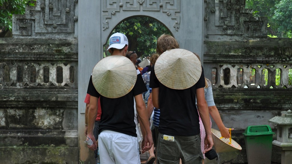Gezin met Vietnamese hoeden wandelt door een tempelpoort tijdens familiereis Vietnam.