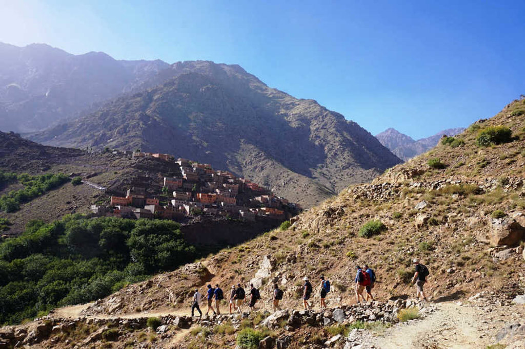 Groep wandelaars op bergpad in het Atlasgebergte bij Mount Toubkal, met dorp tegen de helling in Marokko.
