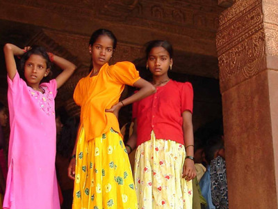 Drie meisjes in kleurrijke kleding onder een gebeeldhouwde tempelboog tijdens de Route Zuid India, 23 dagen.