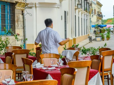Terrasrestaurant in Cuba met gedekte tafels en een ober in een smalle straat.
