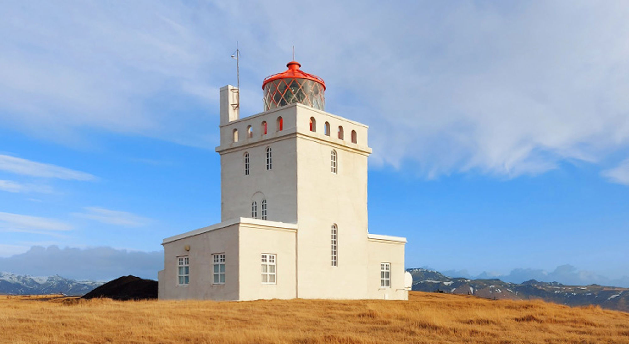 Dyrhólaey vuurtoren Witte vuurtoren op een heuvel in IJsland, met rode lantaarnkamer en bergen op de achtergrond.