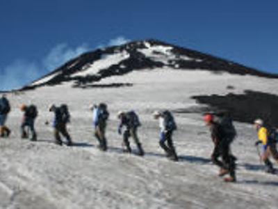 Groep wandelaars op een gletsjerhelling met besneeuwde bergtop op de achtergrond.