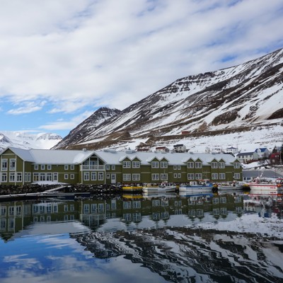 Haven in Noord-IJsland met vissersboten, kleurrijke huizen en besneeuwde bergen op de achtergrond.