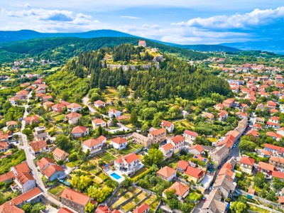 Uitzicht op een Kroatisch dorp met roodtiledaken en een heuvel met fort en kapel, omringd door groen.