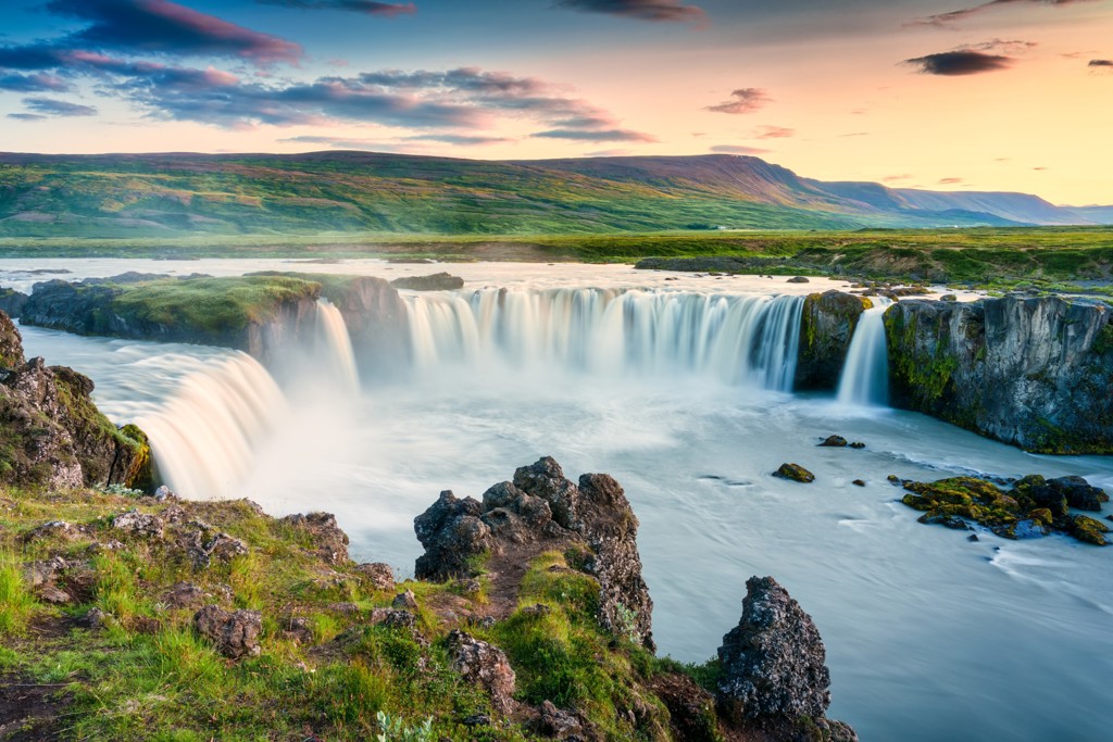 Waterval Godafoss in IJsland bij zonsondergang, met brede waterstroom en rotsachtige oevers.