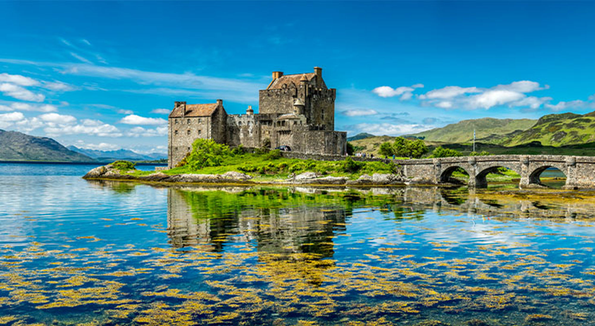 Eilean Donan Kasteel Eilean Donan Castle aan het water met stenen brug en bergen op de achtergrond.