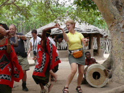 Reizigers dansen met lokale artiesten bij een traditioneel dorp tijdens de Route Zuid-Afrika.