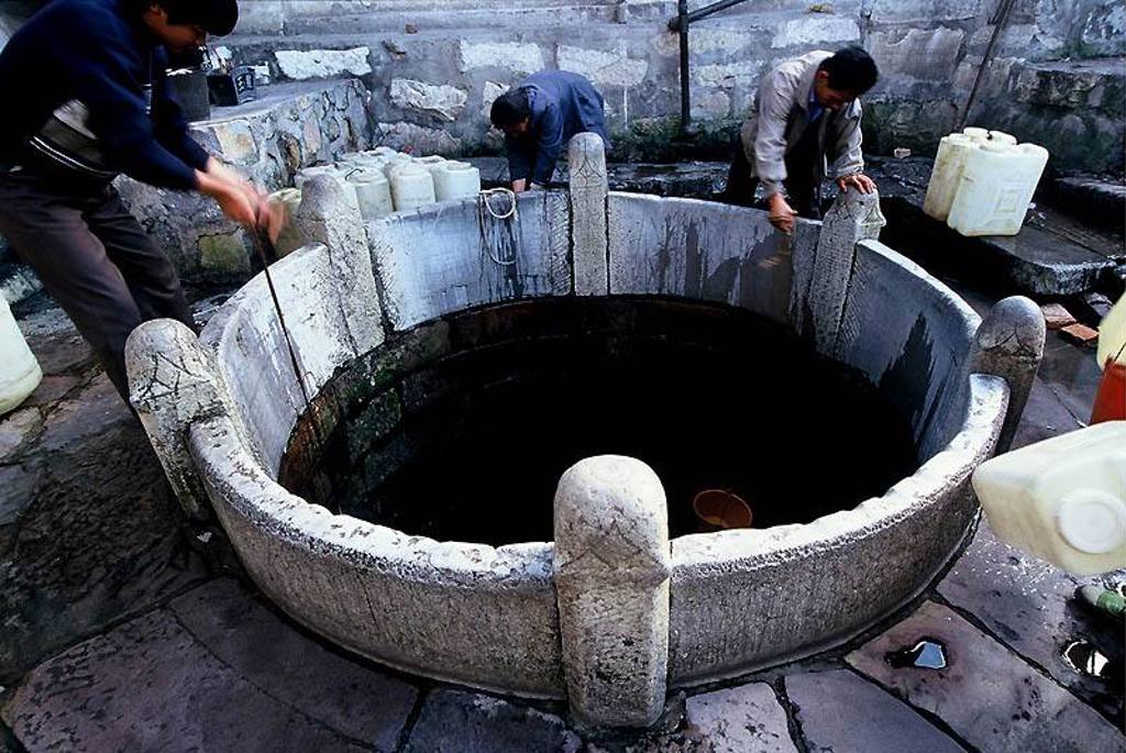 Mannen vullen jerrycans bij een ronde waterput tijdens een groepsrondreis China & Vietnam.