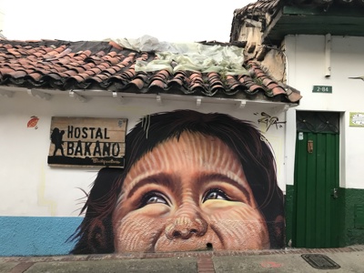 Muurschildering van een gezicht op een wit huis met rood dak en groene deur in Colombia.