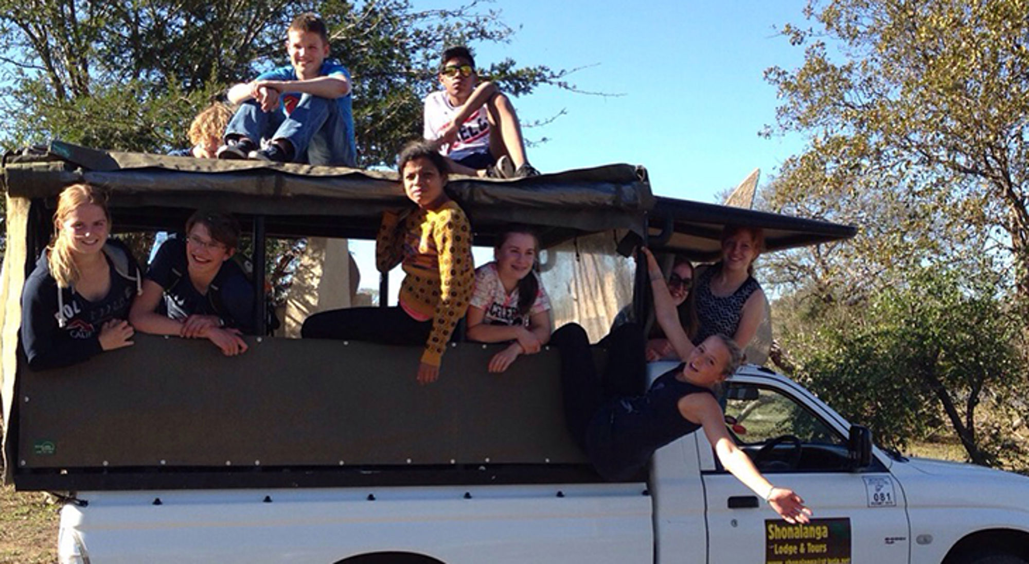 op safari met een truck Groep reizigers in safariwagen tijdens game drive in natuurgebied, met bomen op de achtergrond.