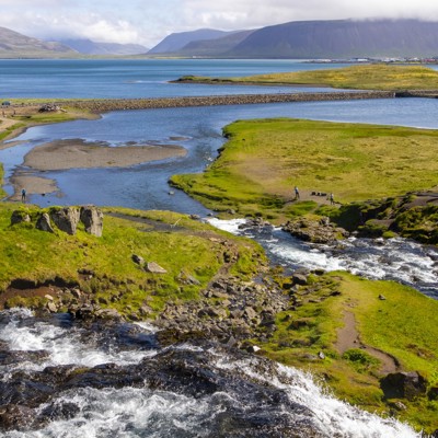 Uitzicht op riviermonding met waterval, groene heuvels en fjordlandschap tijdens groepsrondreis IJsland.