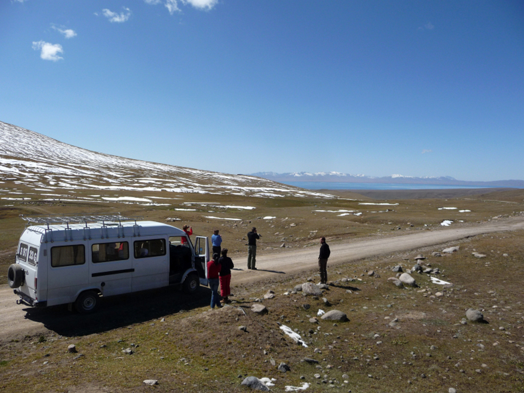 Groepsrondreis Kirgistan: busstop op bergplateau met sneeuwvelden en uitzicht op Issyk-Kulmeer.