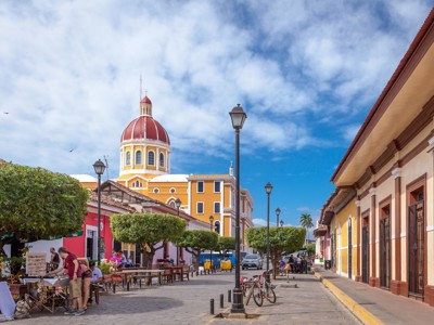 Straatbeeld in Granada, Nicaragua, met de kathedraal met rode koepel en kleurrijke gebouwen onder een blauwe lucht.