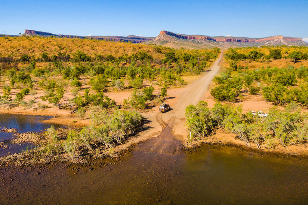 Overland truck op onverharde weg door het landschap van West-Australië, met rivierdoorsteek en rotsformaties.