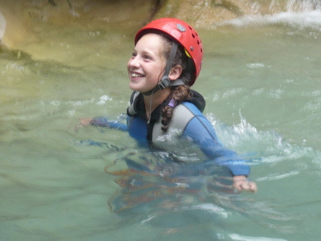 Kind met helm en wetsuit zwemt in een rivier in Mercantour-Vésubie, Frankrijk.
