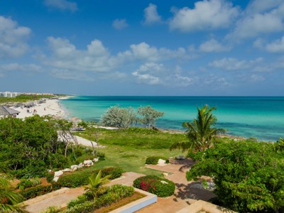 Turquoise zee en wit zandstrand aan de kust van Cuba, omringd door palmen en groen.