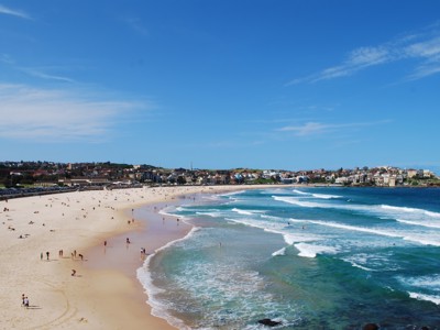 Panorama van Bondi Beach in Sydney met golven, strandgangers en de kustlijn onder een heldere blauwe lucht.