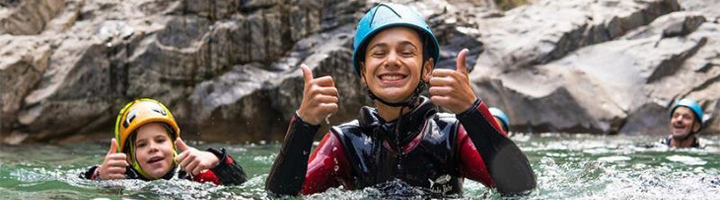Gezin geniet van canyoning in een rivier tussen rotsen, met helmen en wetsuits.